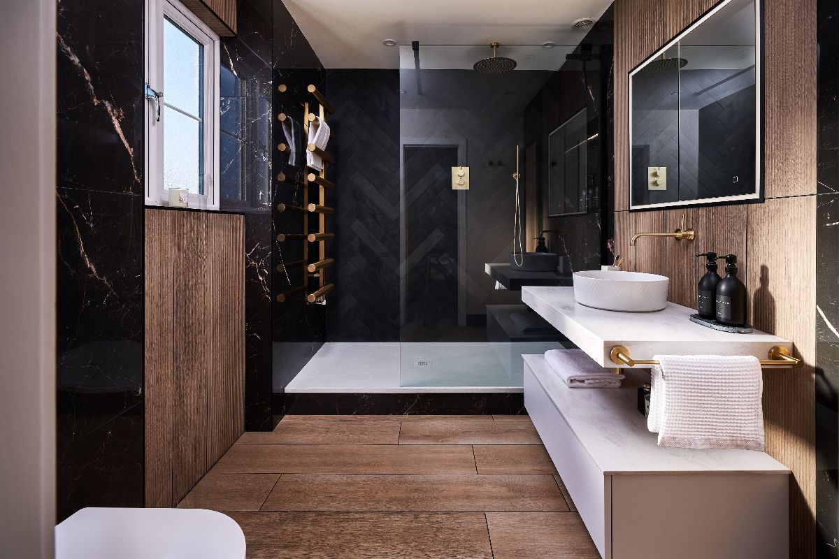 Modern bathroom design with a dark walk-in shower area, wood wall and floor tiles, and an open vanity area with a countertop basin.