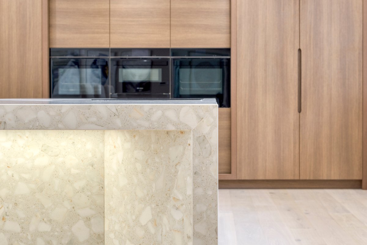 Wood run of cabinetry in the background with built-in appliances, a porcelain-clad island with integrated LED strips.