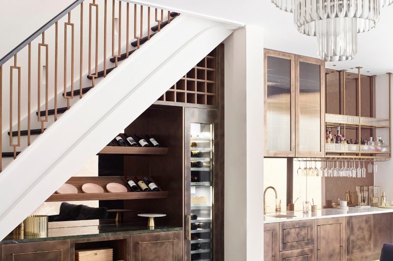A bar area with metallic cabinetry, mirrored splashback, open shelving, and tall fridge.