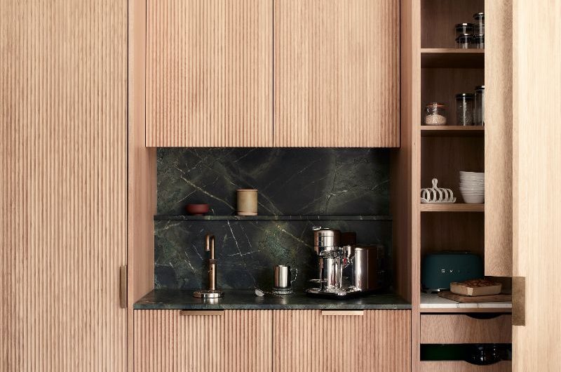 A coffee station with fluted wood cabinetry, green marble and basketweave flooring.