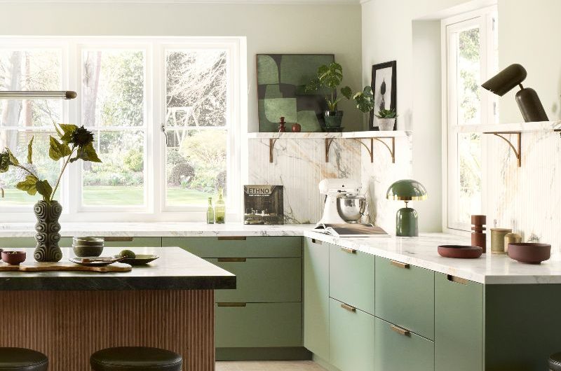 L-shaped cabinetry with a central island, fluted splashbacks, honed worktops, open shelving, and greenery.