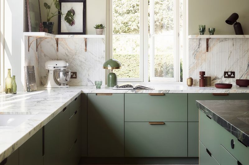 L-shaped kitchen layout with green cabinetry, fluted wood splashback, marble worktop and open shelving.
