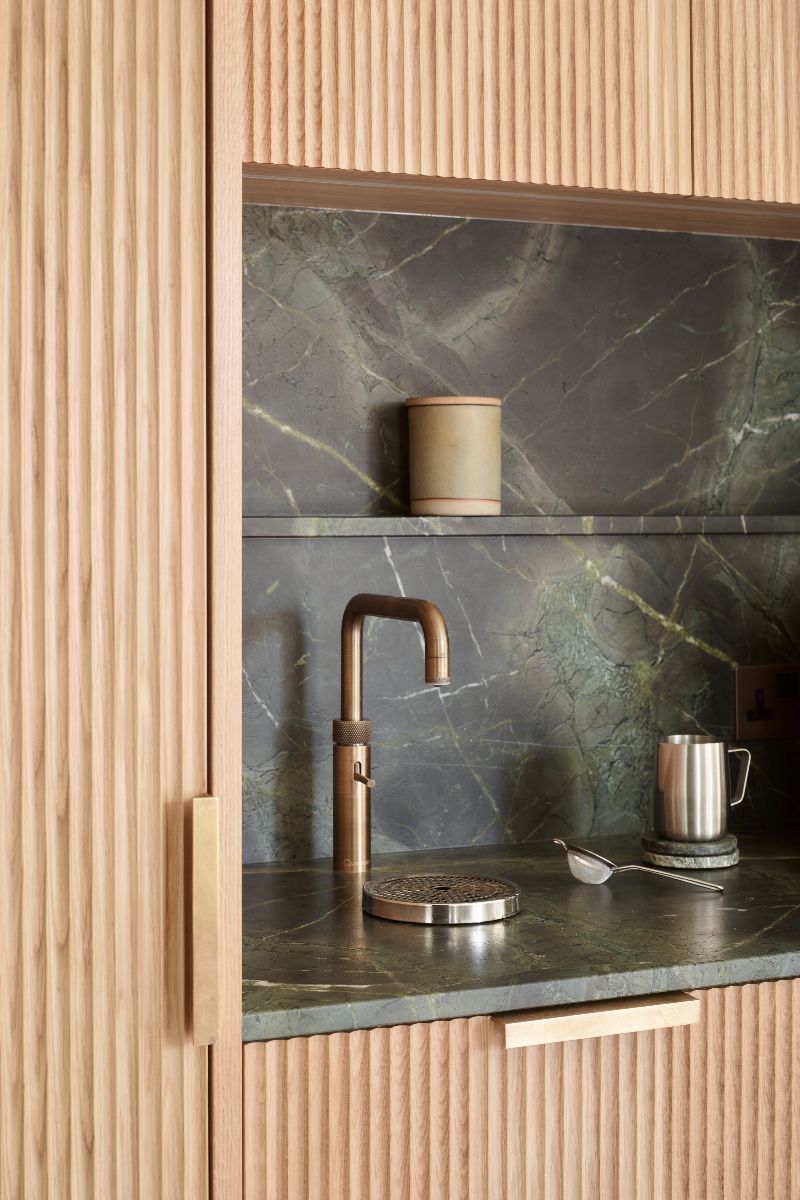 A closeup at a coffee station with fluted wood cabinetry, green marble and a small tap.