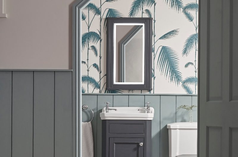 A downstairs cloakroom with blue panelling, patterned wallpaper, classic vanity and mirror cabinet, and timeless toilet.