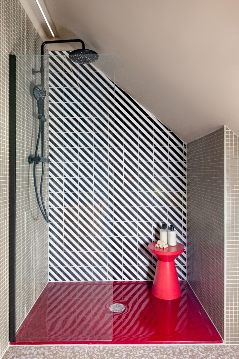 A bold shower design with striped and micro mosaic tiles, black brassware, a pink shower tray and a matching stool for storage.