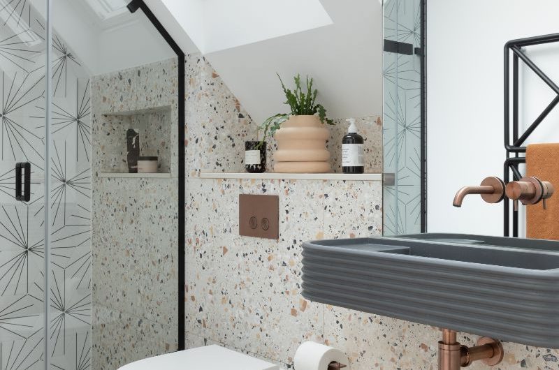 Modern bathroom with terrazzo tiles, a shower area, a concrete basin with industrial brassware and metallic finishes.