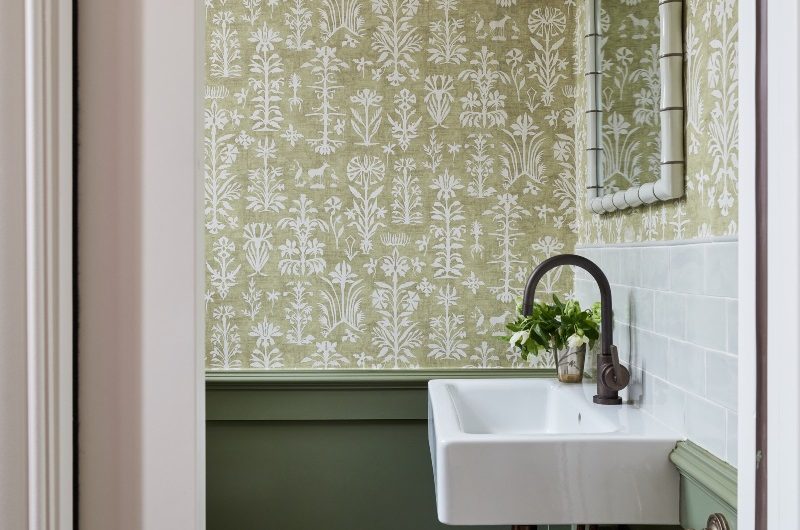 Green bathroom design with patterned wallpaper, green panelling and checkerboard flooring.