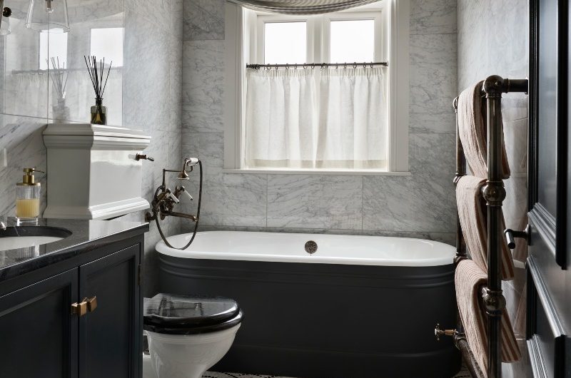 Modern bathroom with a lived-in feel, mosaic floor tiles, dark furniture, matching painted tub, marble wall tiles, and soft furnshings.