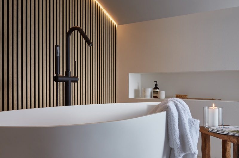 Spa-like space with wood panelling, a white tub, and black bath filler.