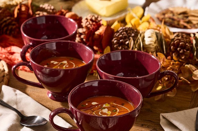 An autumn tablescape with soup in burgundy bowls, linen tea towels, and pine cone garland in the middle.