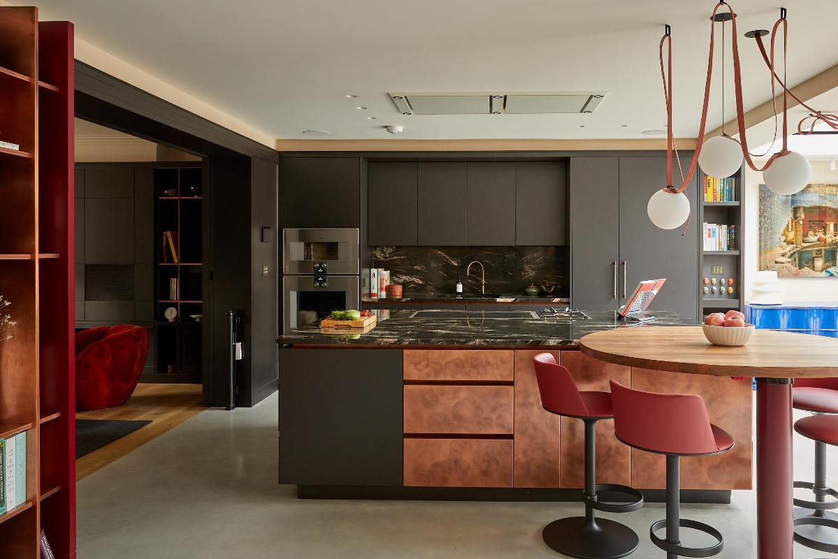 Dark one wall kitchen with a multi-functional island with a built-in dining area, with veiny worksurfaces and copper finishes.