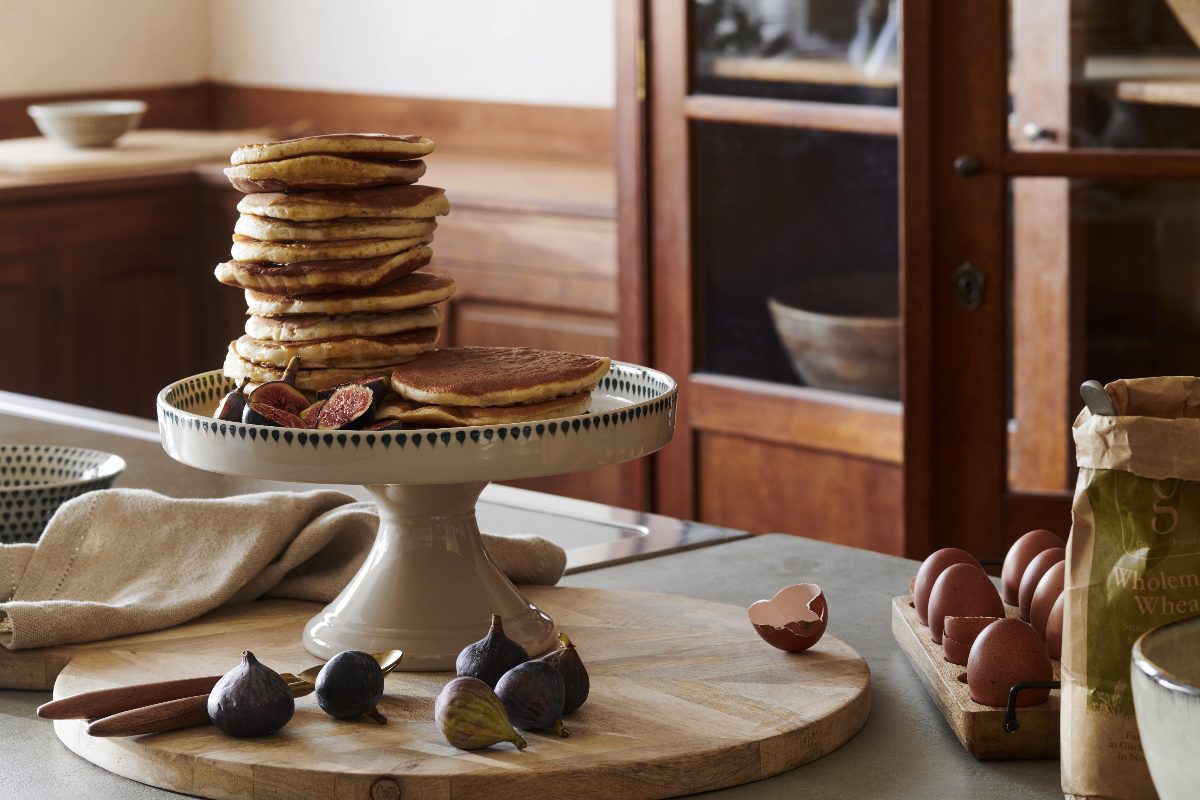An autumn kitchen with a cake stand for pancakes and figs, with baking ingredients next to it.