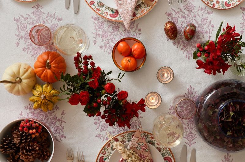 A dining room with classic tablecloth, luxurious crockery, pumpkin decor, red foliage, and simple silverware.