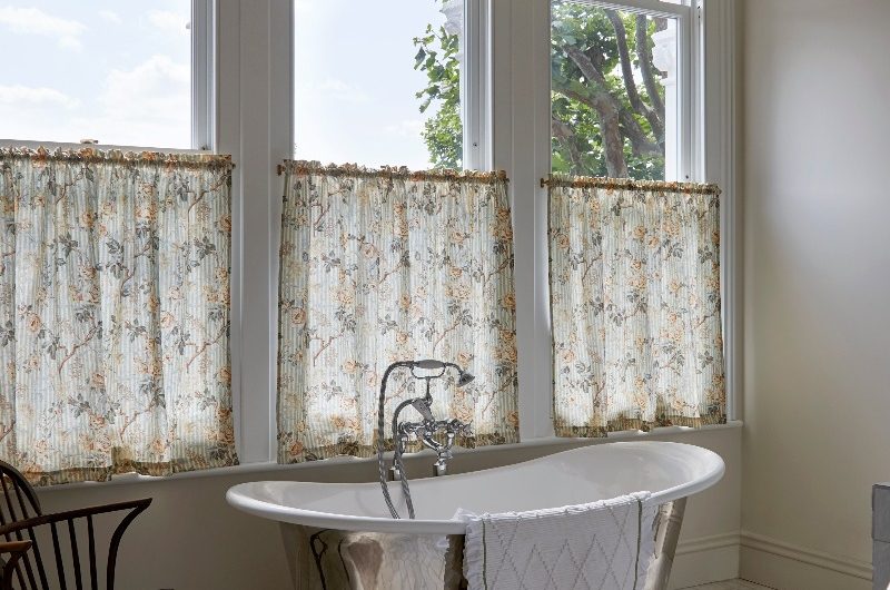 A classic bathroom with a stainless steel tub, herringbone marble flooring, and floral cafe curtains.
