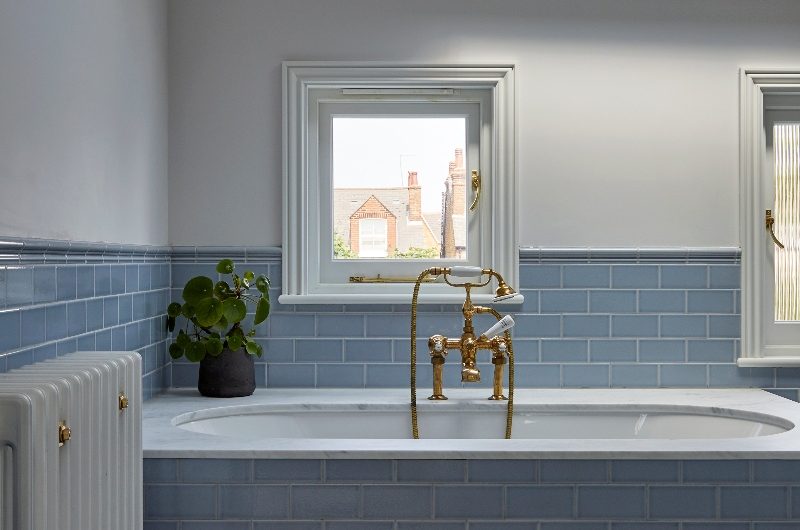 A colourful bathroom with a fitted tub clad in blue metro tiles, black and white checkerboard flooring, and a skylight.