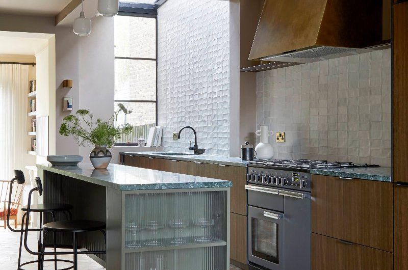 A modern scheme with wood units, topped with green speckled surfaces, a range cooker with a concealed extractor and an island painted in forest green. 