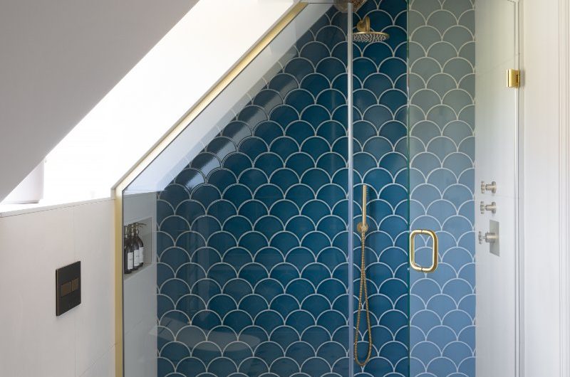 Blue design with a shower area with a brass enclosure, wall-mounted toilet, and a window.