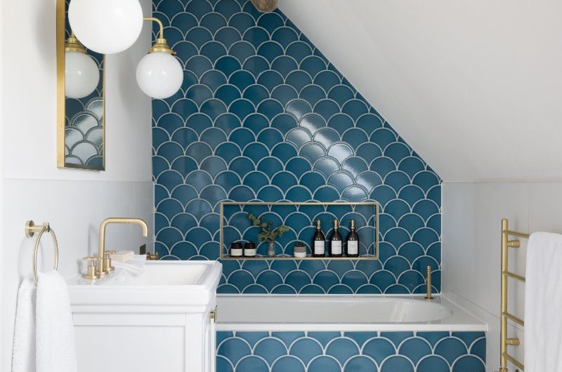 Blue bathroom design with a fitted tub, scalloped tiles, terrazzo flooring, gold accessories and white vanity unit.