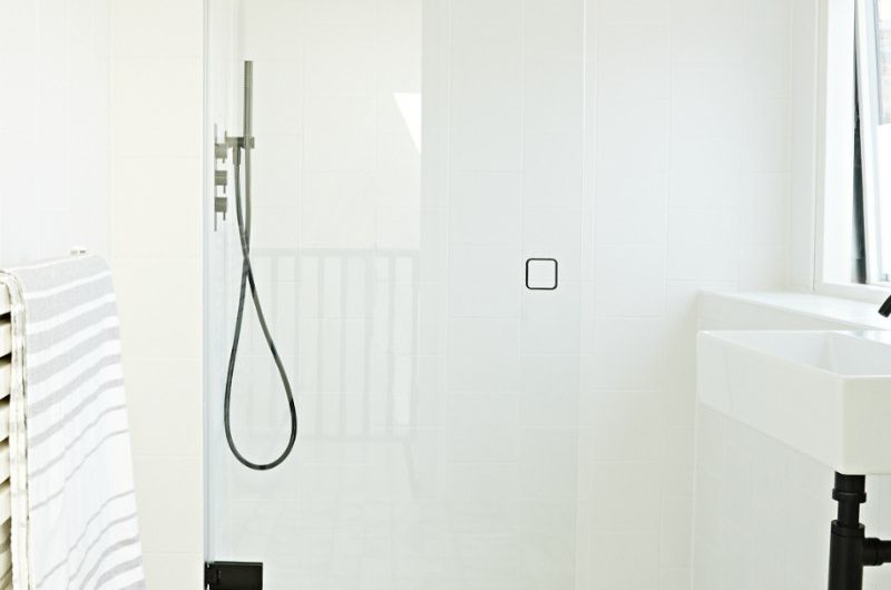 A white bathroom with patterned floor tiles, white walls, white sanitaryware, and black brassware.
