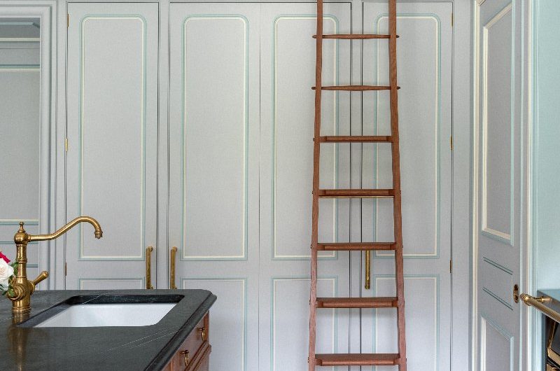 A classic, sophisticated kitchen design with tall cabinetry, a rolling ladder, and a wood island with black worktops.