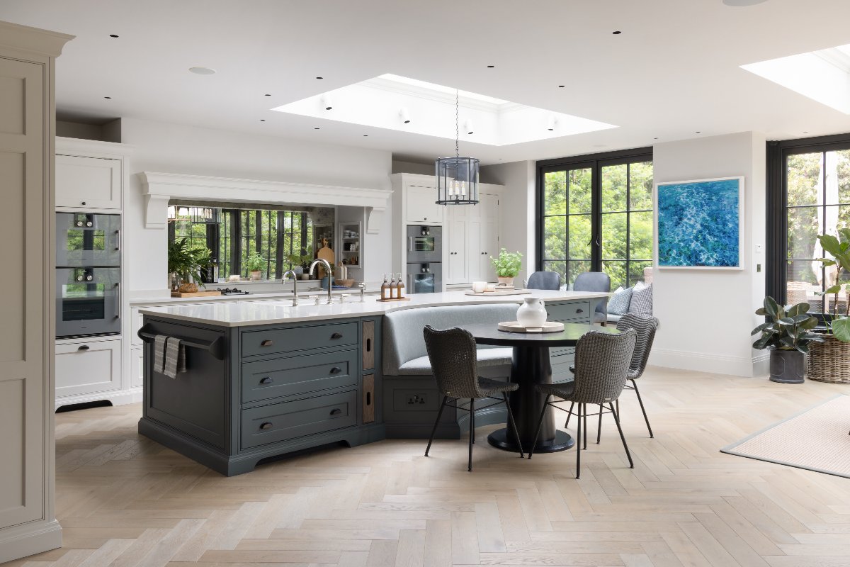 A spacious kitchen with a run of white cabinetry and a central island with storage, a curved bench, dining table and chairs, with a sink zone and a breakfast bar at one end.