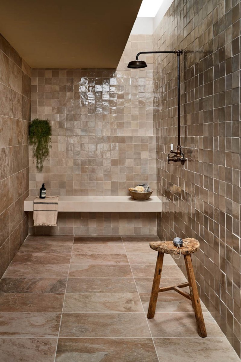 Walk-in shower with neutral zellige tiles on the wall, a shower seat and stone flooring.