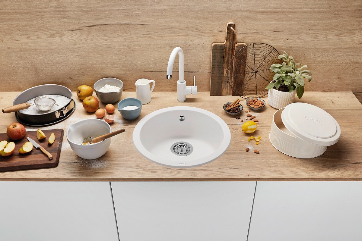 A washing up zone with sleek white units, wood worktop and splashback, and a white sink and tap.