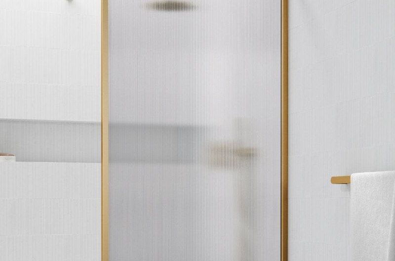 A luxurious bathroom with a gold framed panel, marble flooring and a skylight above it.