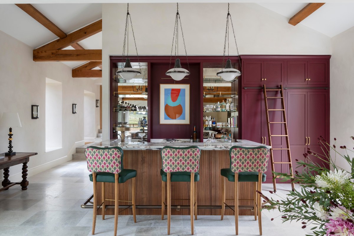A burgundy kitchen with a bar area, a central island with fluting, and a rolling ladder to access the tall cupboards.