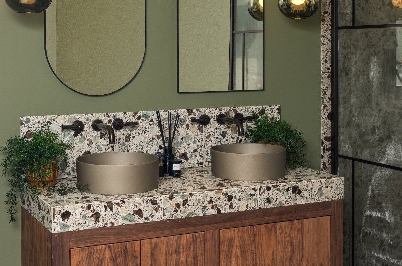 Nature-inspired spa-like space with wood flooring and furniture, double basins, speckled surfaces, green paint on the walls and minimalist, sleek decor.