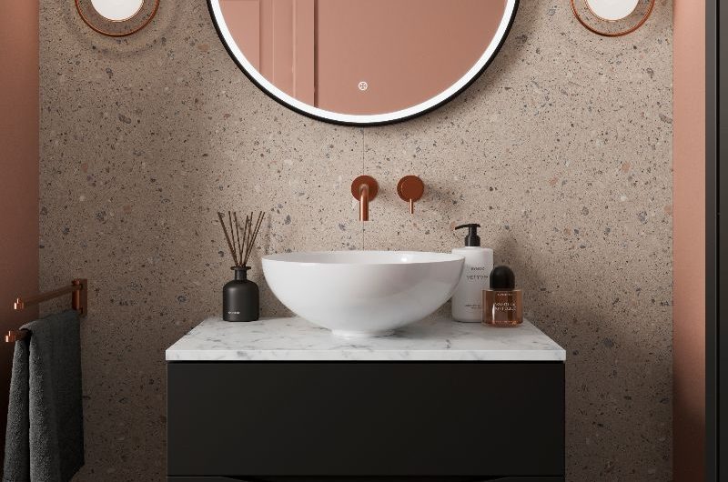 Modern bathroom vanity area with a dark base, marble worktop, countertop basin, circular mirror, and copper accents.