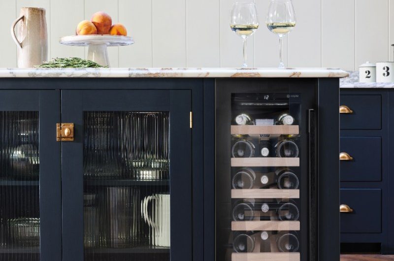A navy kitchen design with classic cabinetry and a central island with glass cupboards and a small drinks fridge.