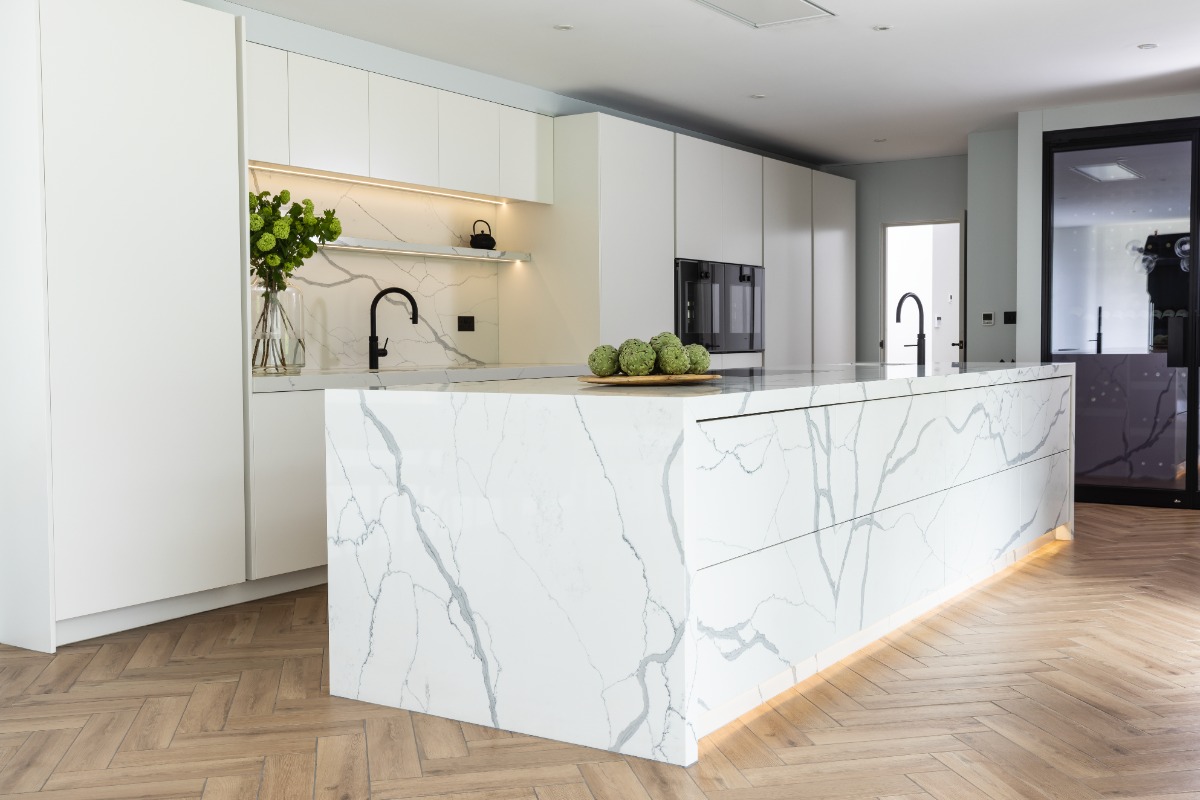 A modern cooking space with handleless white units and a bookmatched island with veiny surfaces and LED plinth lighting.