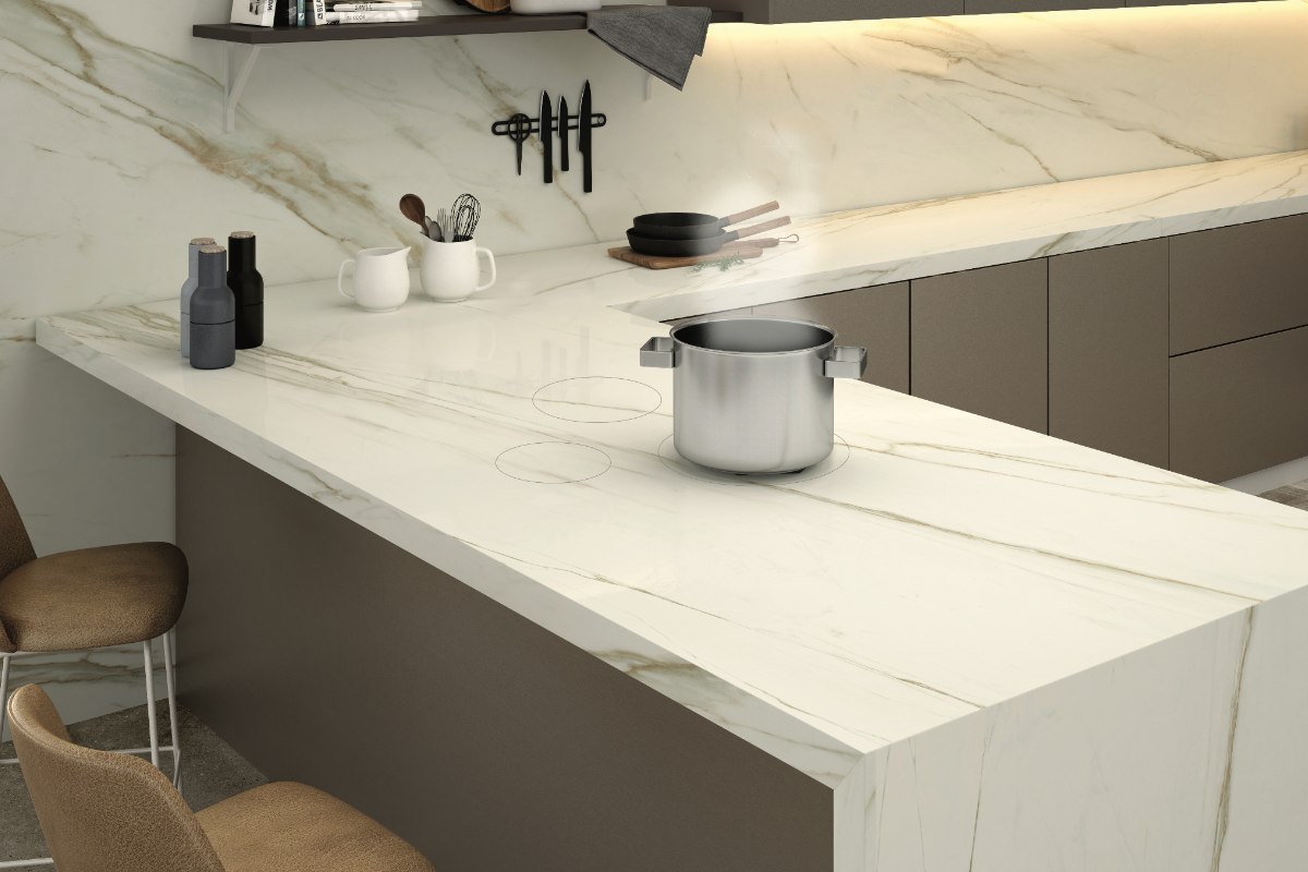 An L-shape cabinetry run with an invisible hob, storage, and breakfast bar. The cabinets are handleless and painted in a neutral colour, topped with veined surfaces.