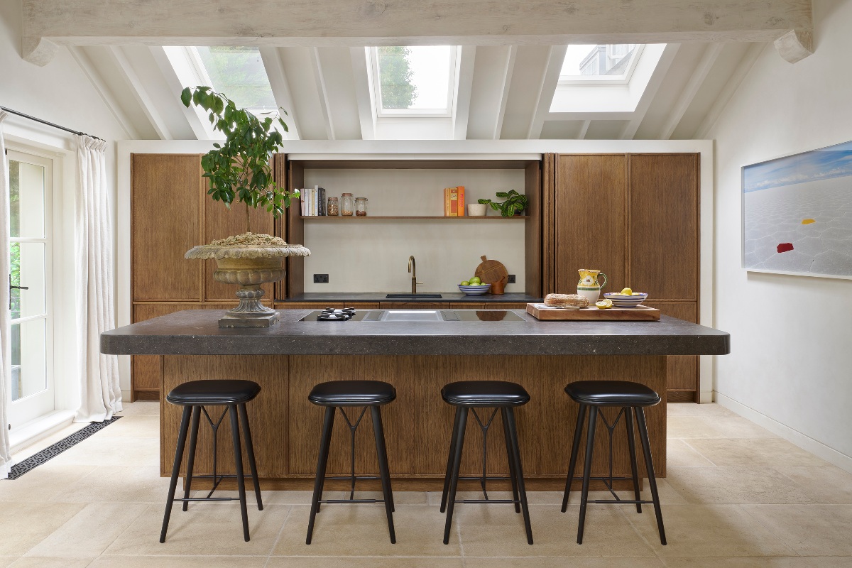 A Scandi style kitchen design with wood cabinets, a central island with dark stone worktop, hob, and seating, and skylights flooding the space with light.