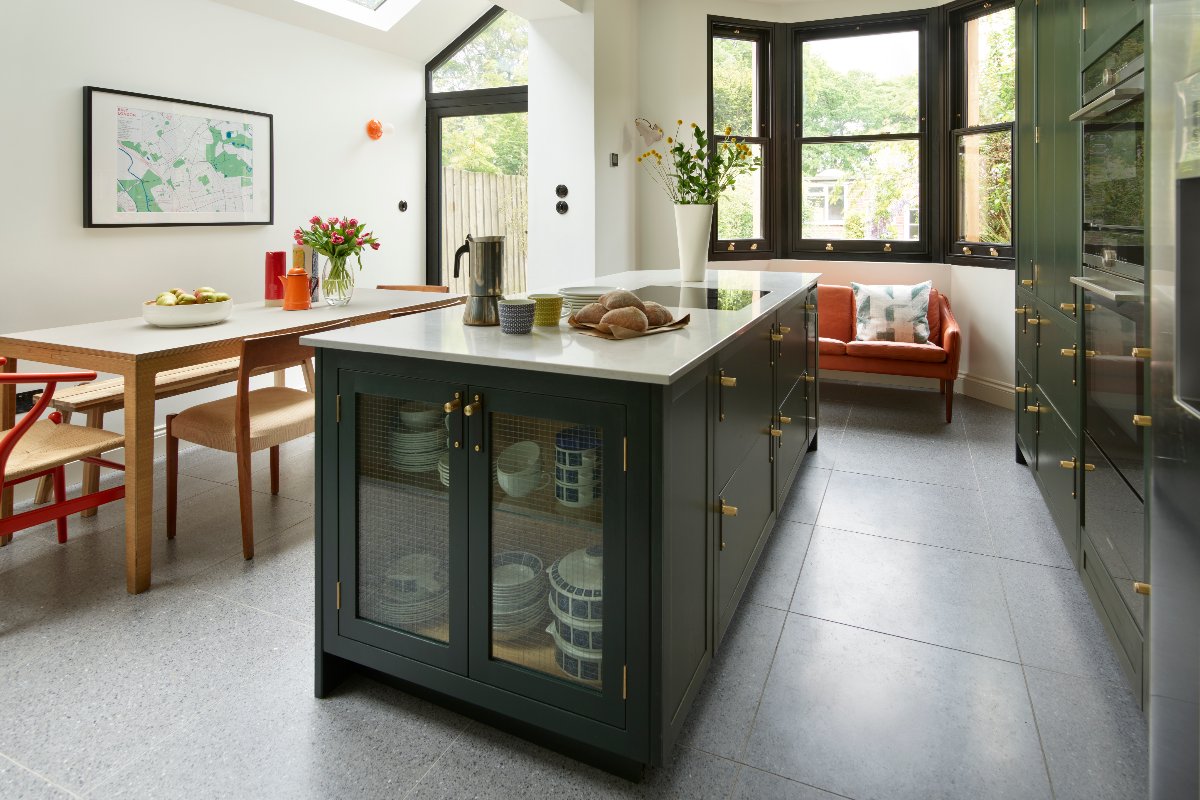 A contemporary kitchen design with a central unit with storage and a hob, a dining area, and steel-framed glazing.