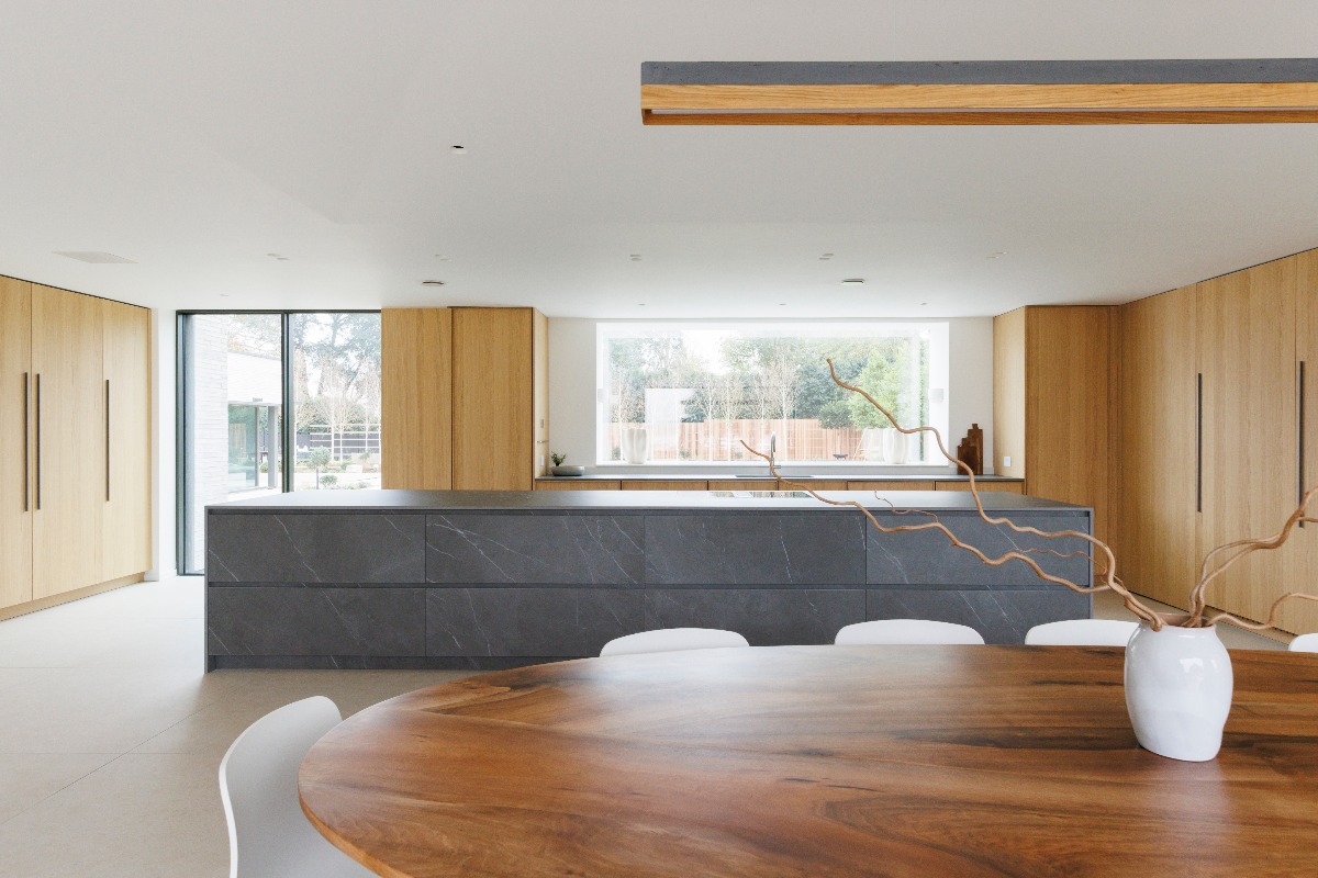 A grand open-plan room surrounded by tall wood cabinets with a central stone-clad unit with an induction hob.