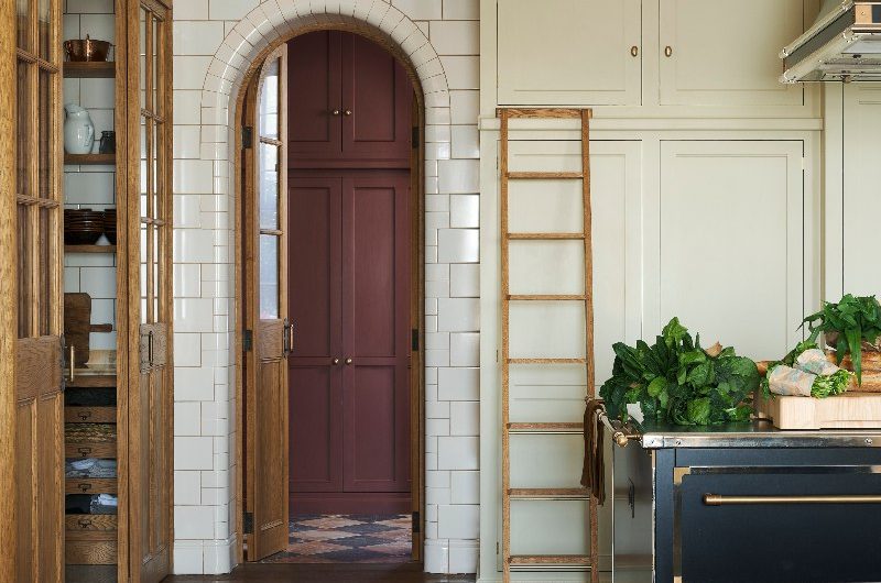 A classic kitchen design with cream cabinetry, a blue island, and an adjoining pantry.