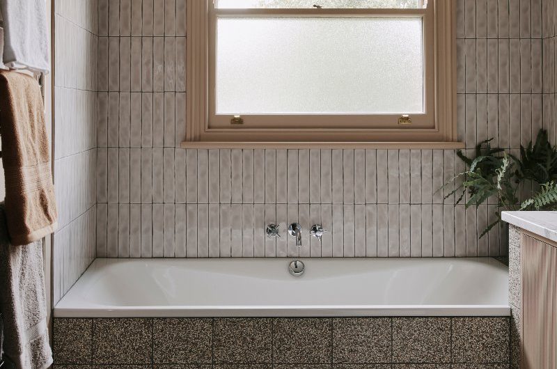 Neutral bathroom with glossy white metro tiles on the wall, speckled flooring, neutral furnishings, and house plants.