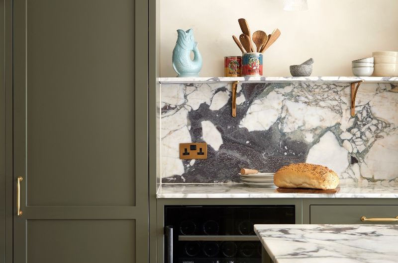 Closeup at dark green cabinetry, Calacatta Monet marble, built-in wine fridge and brass detailing on hardware and power sockets.