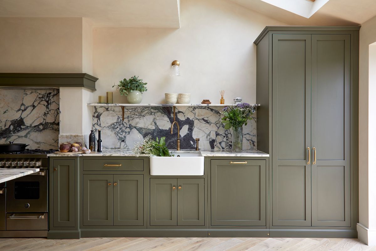A washing up area with a butler sink, brass tap, marble worktop and splashback, and a matching shelf for displaying decor.