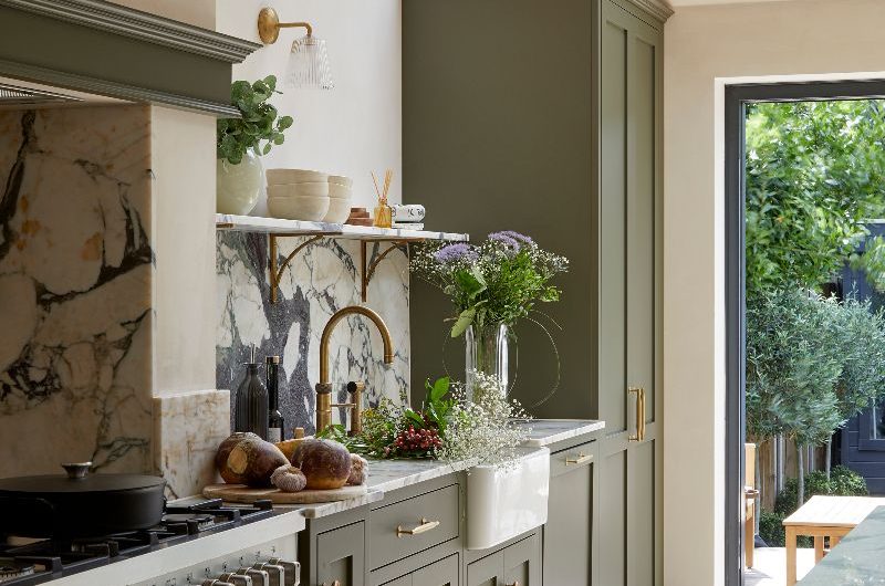 The dark green kitchen with statement marble surfaces, classic cabinets and wood flooring, looks out onto the garden.