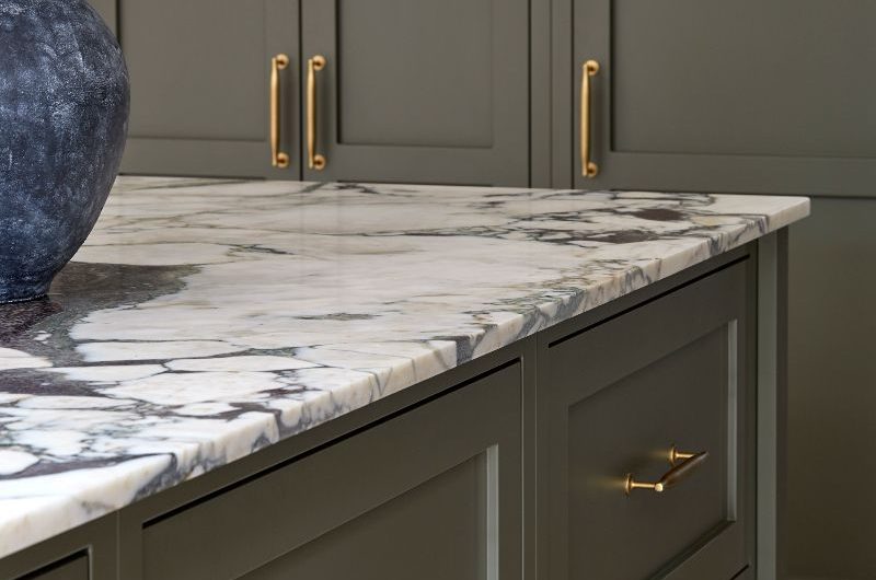 A dark green kitchen island with deep drawers and marble worktop.