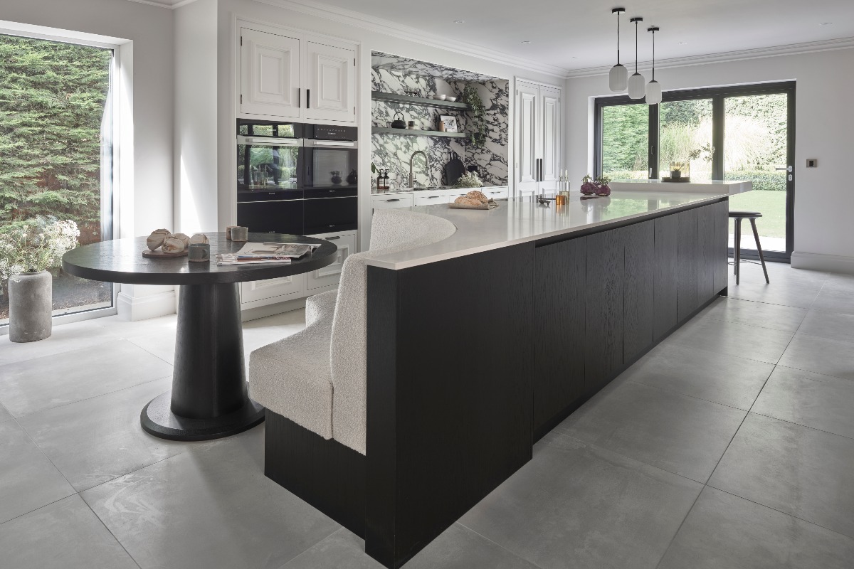 An extra large kitchen island with a high breakfast bar seating area and a low circular booth section near a breakfast pantry.