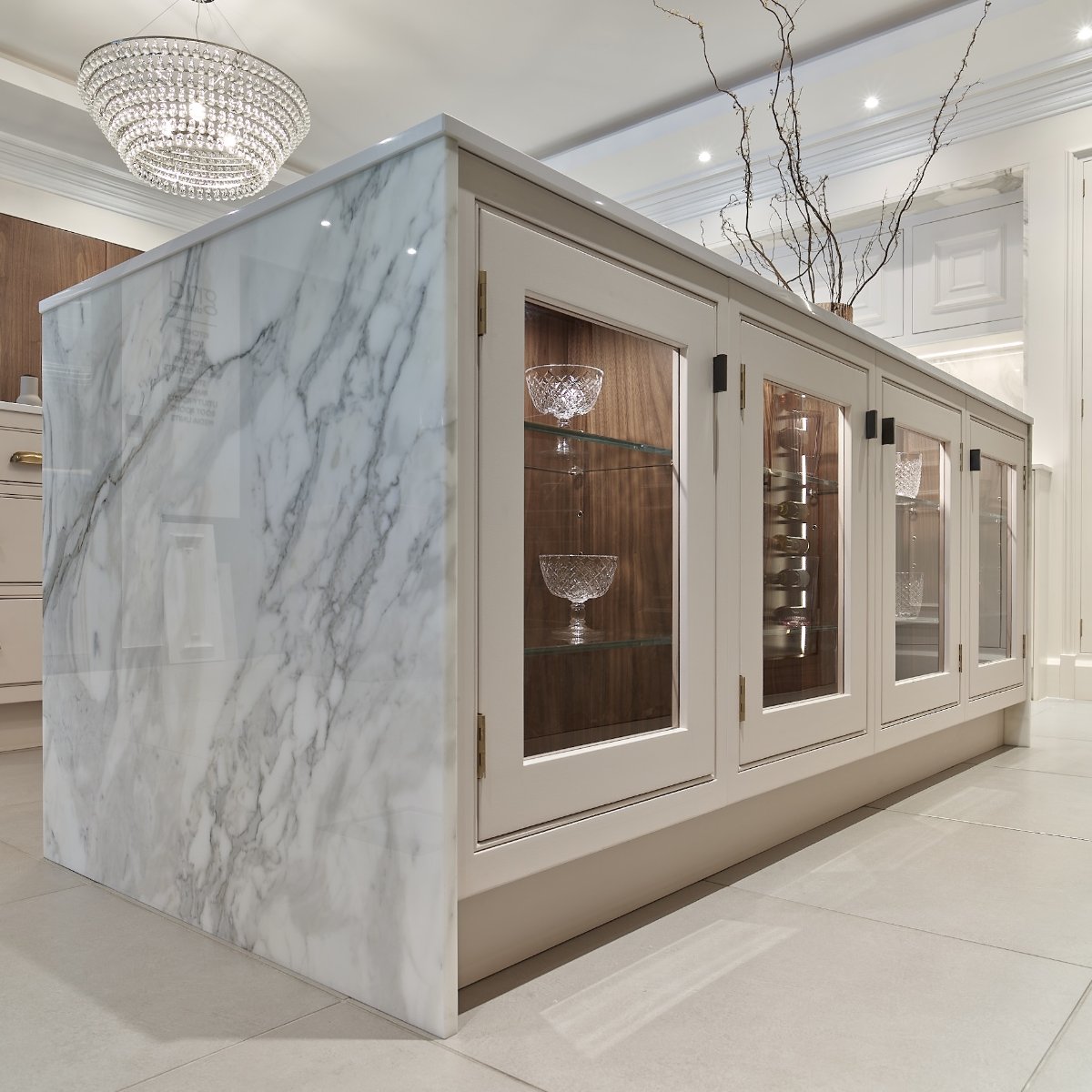 Classic kitchen design with veiny work surfaces and an island with display cabinets with built-in lighting and wood interiors. 