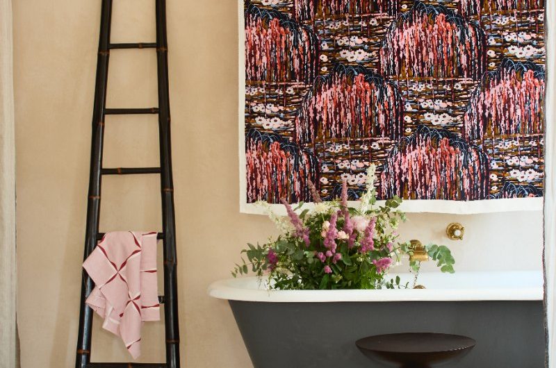 A calm, elegant bathroom with a painted tub, wall textiles, a jute rug, and accent side table.
