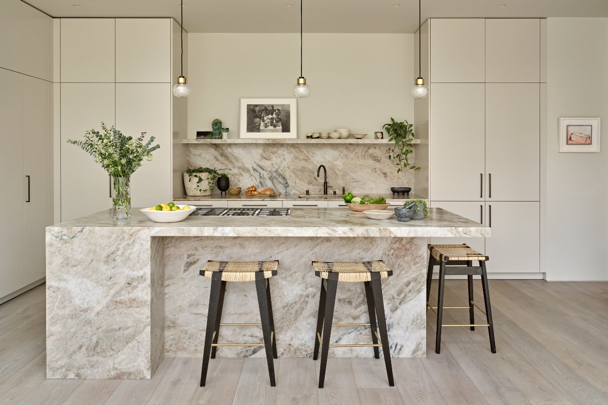 A neutral L-shaped kitchen design with floor-to-ceiling cabinetry, stone surfaces, a central island with a breakfast bar and compact pendants above the unit.
