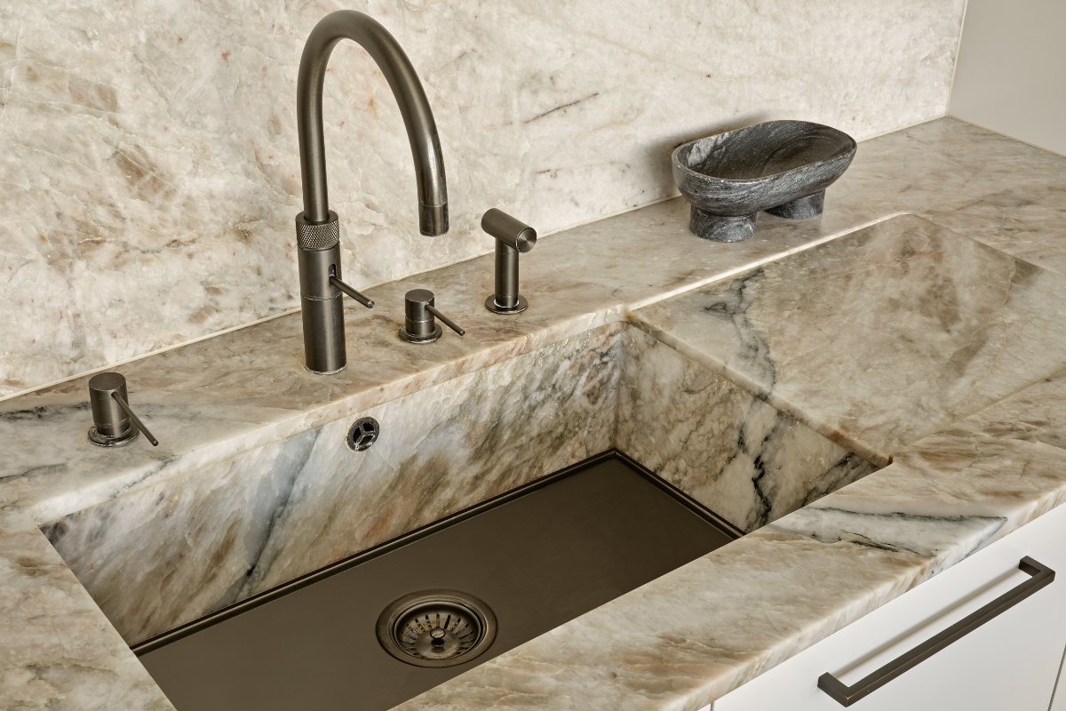 A sink ares with edges crafted from the same stone as the worktop, with a gunmetal tap and minimalist decor.
