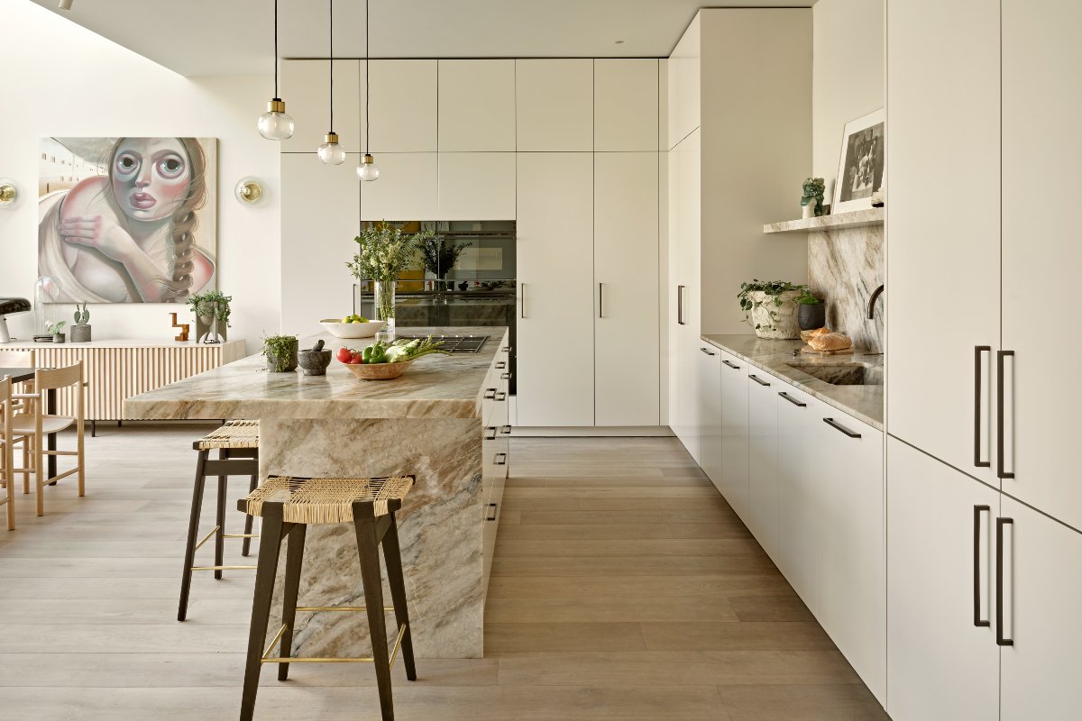 View of the L-shaped cabinetry painted in a neutral tone with a central stone island and built-in appliances.