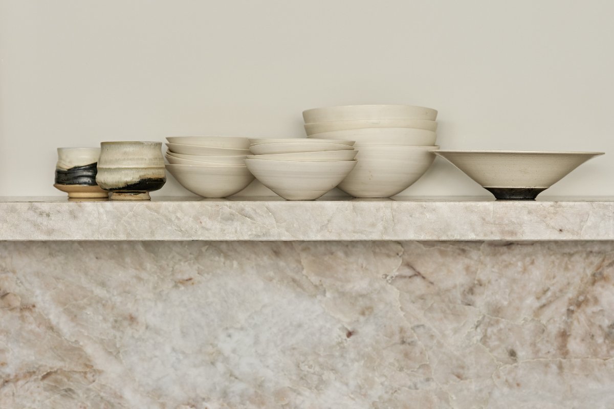 An open shelf made from the same stone as the splashback with white crockery on display.